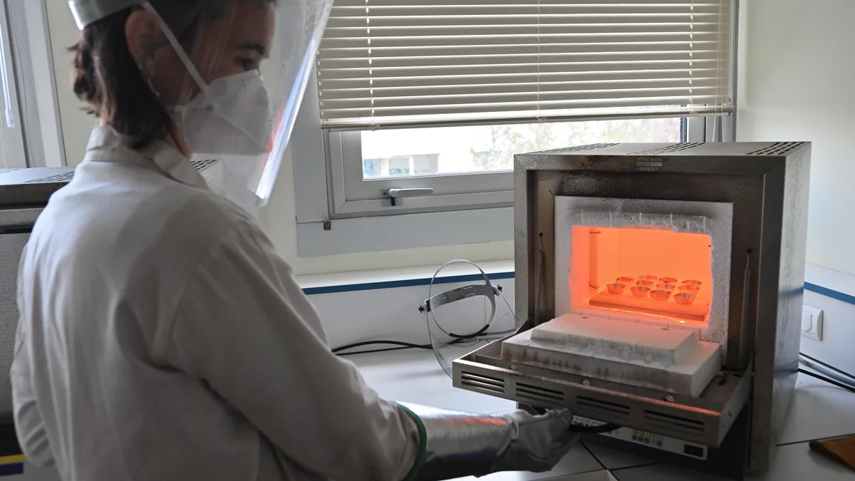 Laboratory technician handling rock samples in a high-temperature furnace during XRF sample preparation
